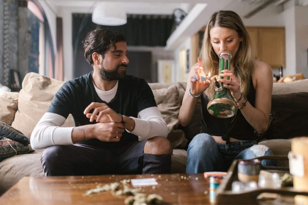 A man and woman smoking marijuana on a couch, using a dab pen.