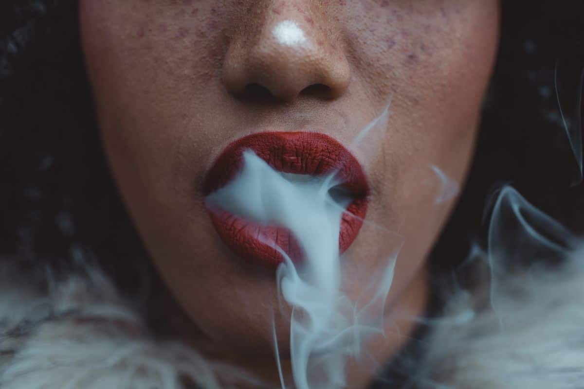 A woman smoking ghost extracts e-cigarette with red lips.