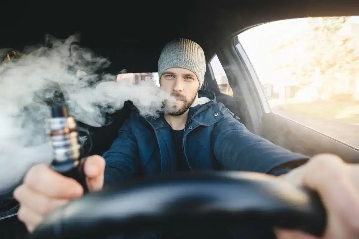 A guy driving a car and vaping at the same time