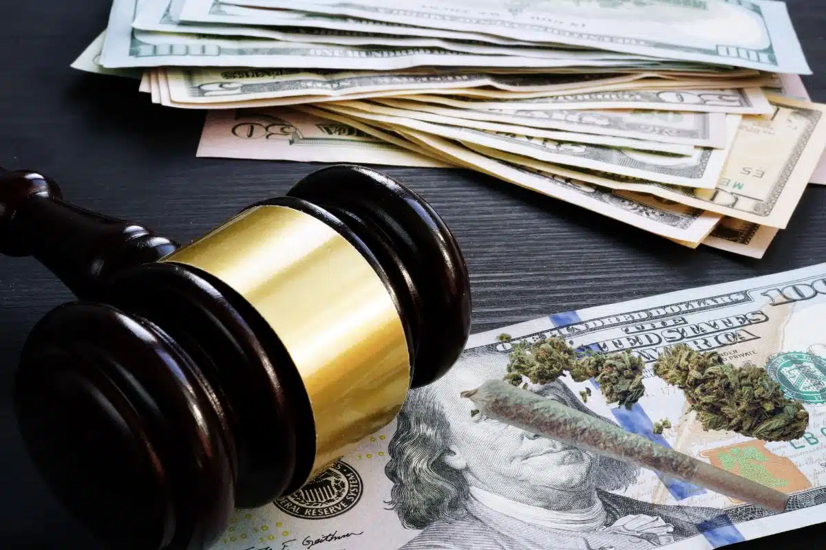 A wooden gavel sits on top of a pile of money and joint beside it