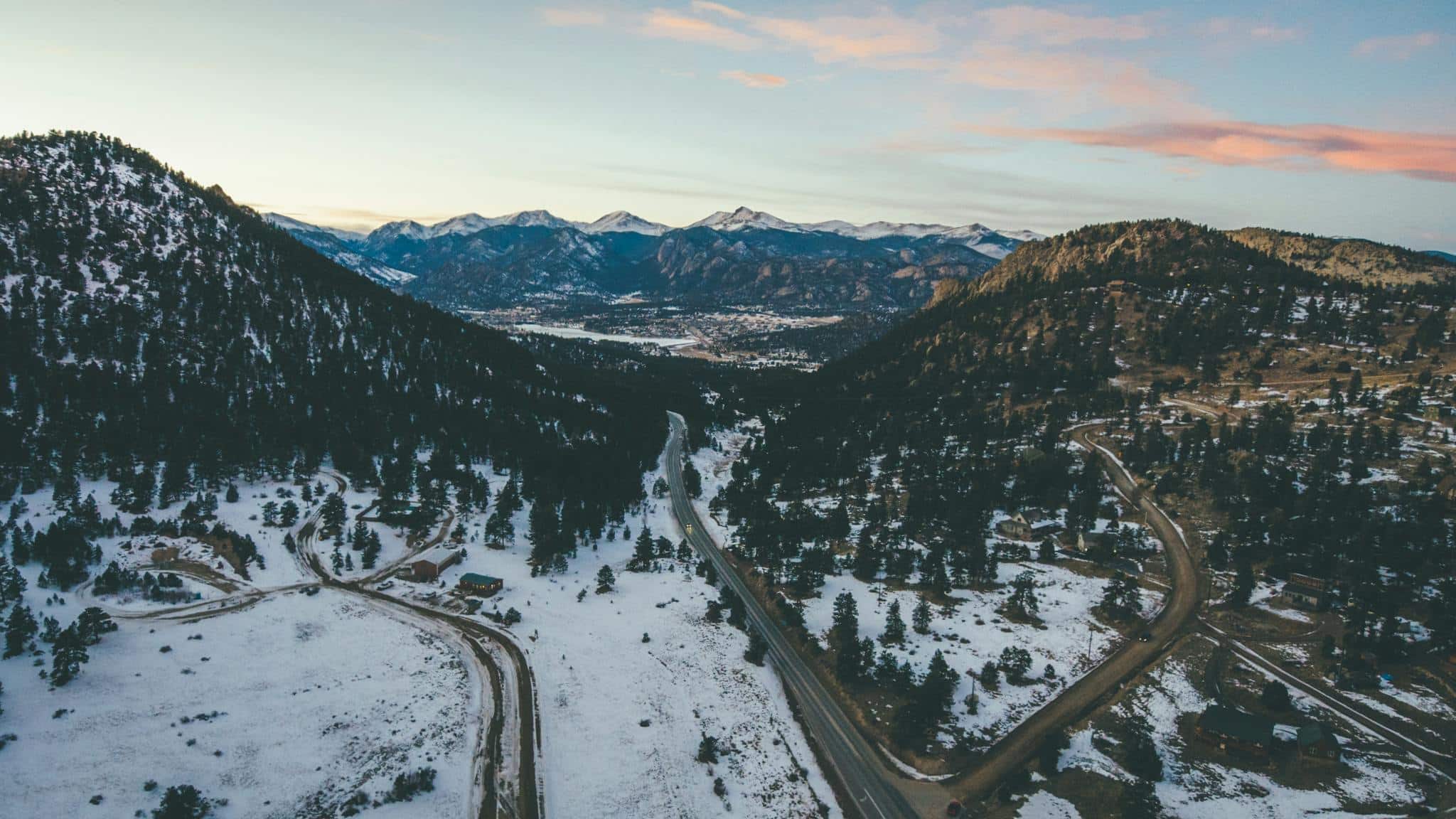 Aerial View of Road Between Trees and colorado Mountains