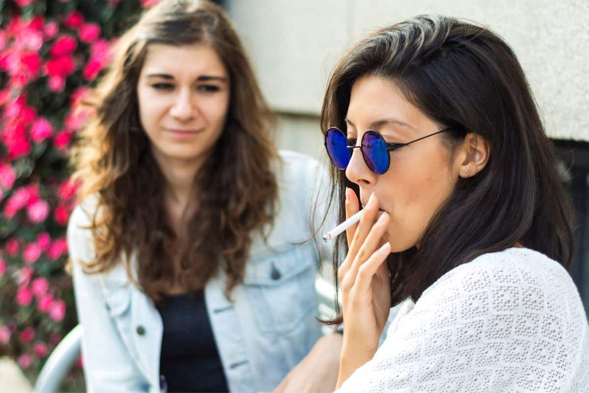 Two women sharing a spliff while sitting on a bench.