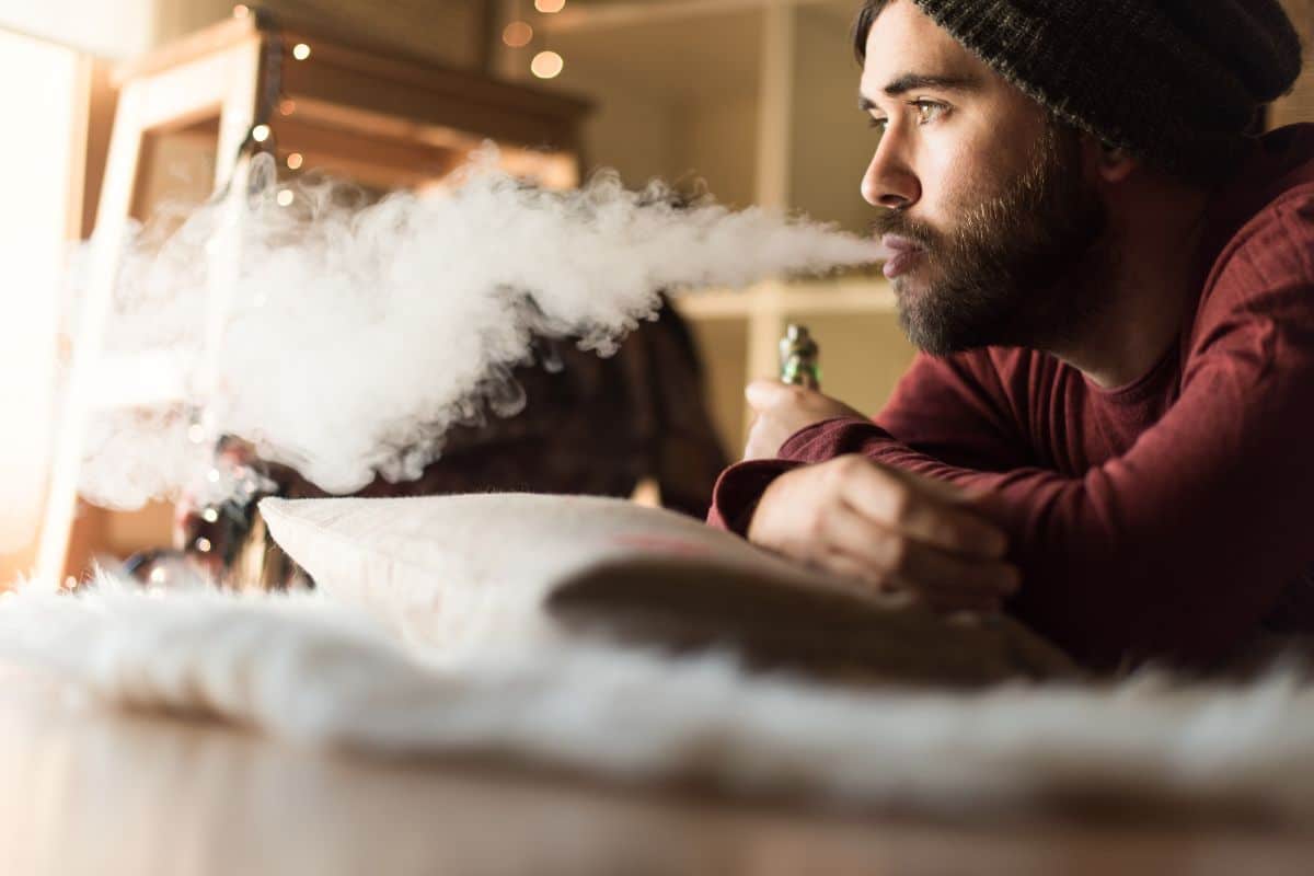 A guy vaping after removal of his wisdom tooth and relaxing at home.