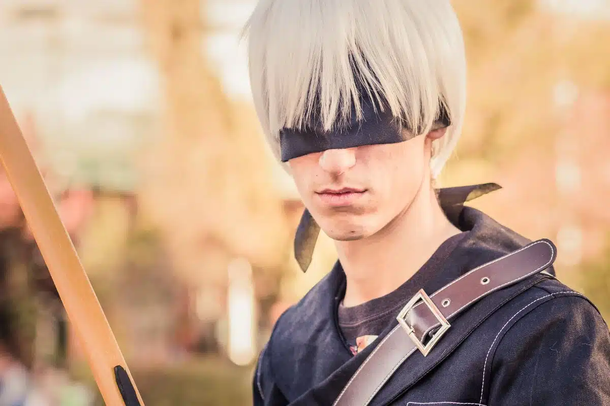 Person in cosplay with a blindfold and white wig, holding a bow, reminiscent of the best anime about weed.