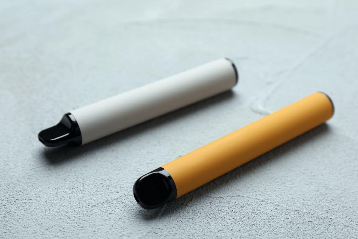 Two popular disposable electronic cigarettes lying on a textured surface.