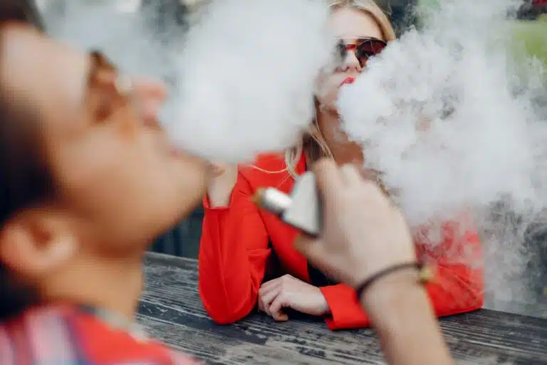 Two individuals exhaling vapor from the highest nicotine vapes outdoors.