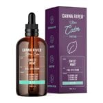 A bottle and box of Canna River CBD Ultra Calm Tincture are displayed. The label highlights a refreshing Sweet Mint flavor, full spectrum, and 15,000mg CBD. The box features similar branding with a leaf graphic and mentions lab-tested and cruelty-free qualities.