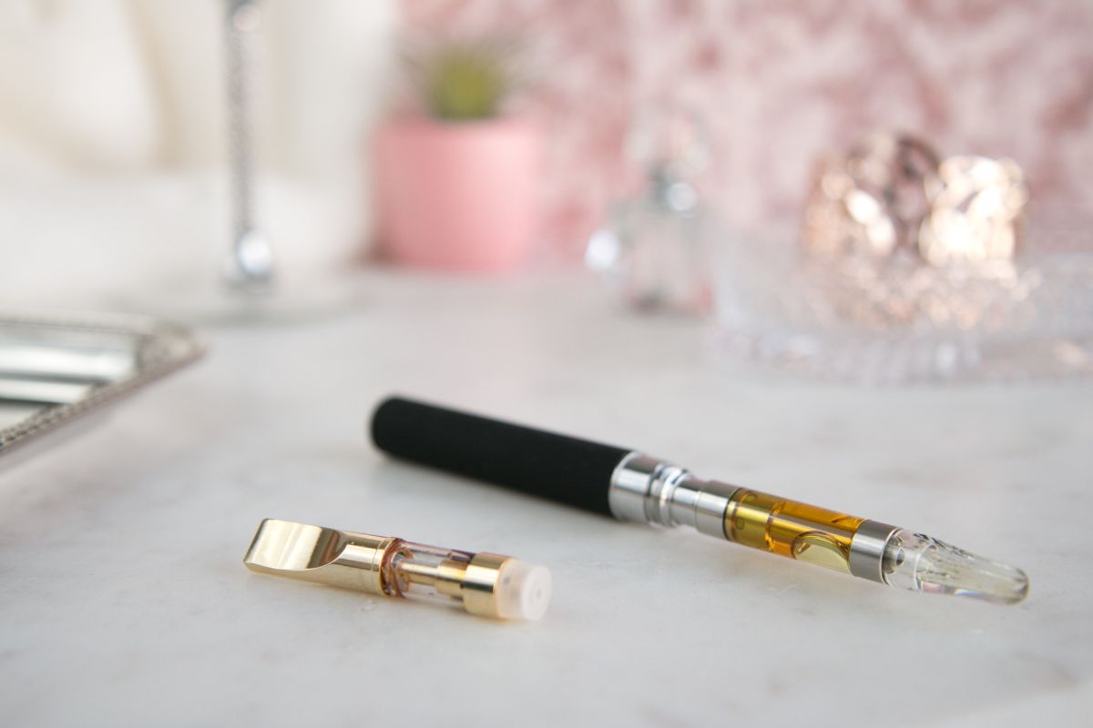 A vape pen with a black handle and a golden cartridge sits on a marble surface, making one wonder, Why does my cart oil move fast